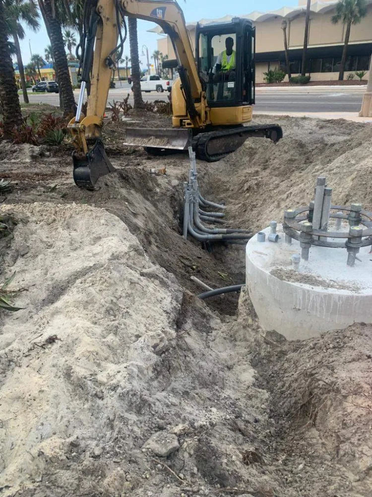Mini excavator opening a trench alongside a conduit bank and foundation
